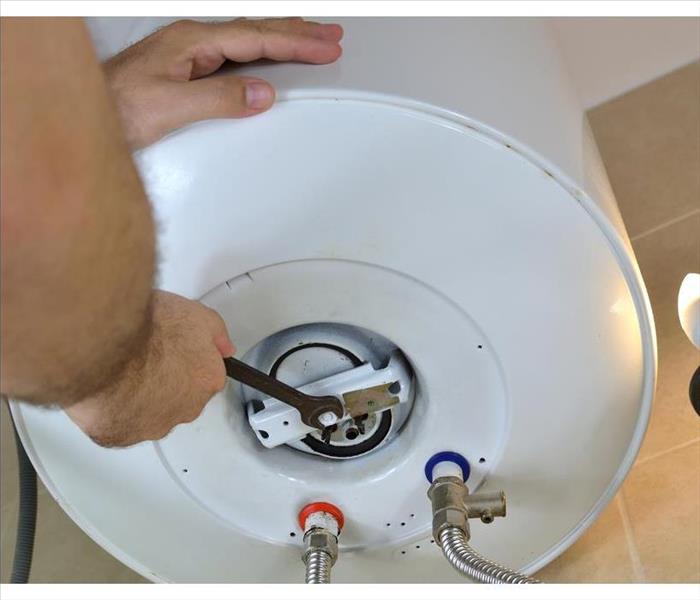 Man's hands unscrewing a screw-nut on a water heater with a wrench on a boiler.