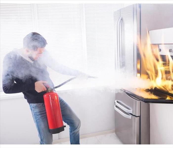 A young man is extinguishing a fire in a kitchen